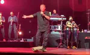 A band performs on stage with a lead singer in a black shirt holding a microphone and gesturing.