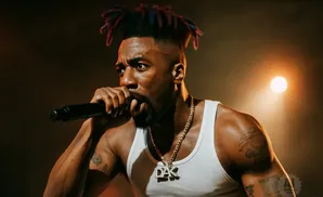 Rapper performs on stage in a white tank top, holding a microphone and wearing a gold chain with 