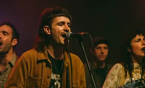 A band performs on stage with a lead singer in the foreground.
