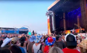 Crowd at an outdoor concert with a large stage and Ferris wheel in the background.