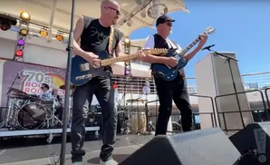 Two men play guitars on a stage with a 