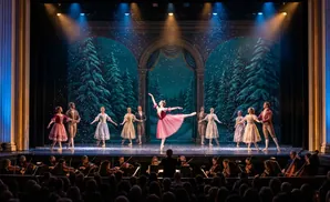 Ballet dancers perform on a stage decorated with snowy trees, while an orchestra plays in front of a seated audience.