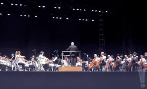 An orchestra performs on a stage, with a conductor leading them.