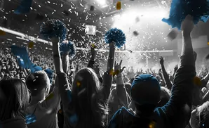 A crowd cheers at a concert or sporting event, with blue pom-poms, confetti, and some golden accents.