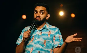 A man in a Hawaiian shirt holds a microphone and gestures with his free hand.