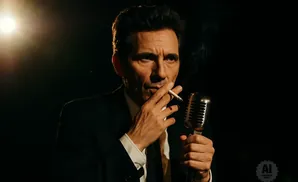 Man in a suit and tie, smoking a cigarette and holding a vintage microphone.
