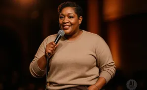 A Black woman with short hair smiles while holding a microphone on a stage.