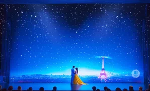 A couple dances under a starry sky in front of a projection of the Eiffel Tower and Paris.