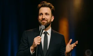 A man in a suit holds a microphone and gestures with his hand while speaking.