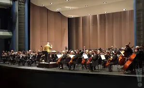 Orchestra performing on stage with a conductor leading them.