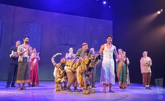 A cast celebrates on stage with a tiger puppet in a theatrical production.