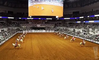 Riders on horseback with flags parade in an arena before a large crowd.