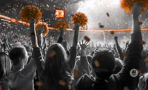 Crowd at a sporting event holding orange pom-poms, with confetti falling.