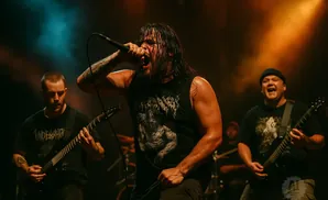 A heavy metal band performs on stage with a vocalist front and center, while two guitarists play behind him.