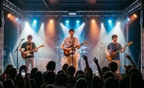 A band performs live on stage with bright lights and a crowd in the foreground.