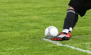 Soccer player's leg and foot about to kick a ball on a green field next to a white line.