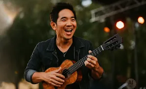 A man with an open mouth smiles while playing a ukulele.