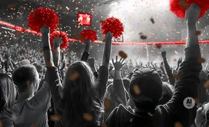 A crowd cheers, holding up red pom-poms amidst falling confetti.