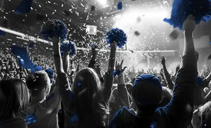 Crowd cheering at a concert with blue confetti and pom-poms.