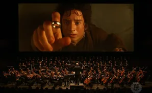A film scene with Frodo holding the One Ring plays above a live orchestra.