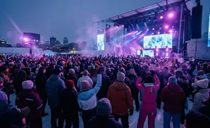 Crowd watching a concert on an outdoor stage at night, with snow falling.