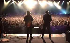 Two men in cowboy hats on stage in front of a large, cheering crowd at a concert.