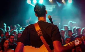 A guitarist performs for a cheering crowd under bright stage lights.