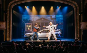 Stage musical performance with actors in 1950s attire, a clock tower, and a DeLorean car.