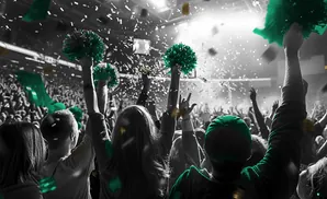 Crowd cheering at a concert with green pom-poms and confetti.