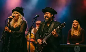 A band performs on stage with singers and a guitarist.