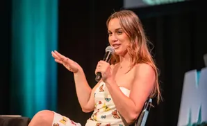 A woman in a strapless dress with butterflies on it holds a microphone and gestures with her hand.