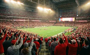A packed stadium with fans in orange and purple cheering on a football game at night.