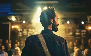 A guitarist on stage looks out at the audience, illuminated by a spotlight.
