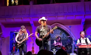 A country rock band performs on a dimly lit stage with purple lighting.