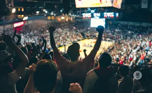 Fans cheer with fists raised at a crowded basketball game.