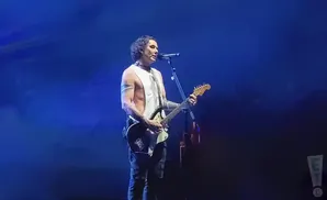 Singer and guitarist on stage, bathed in blue light, playing a black electric guitar.