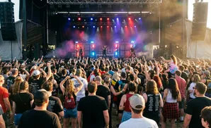 A band performs on a stage at an outdoor music festival to a large, cheering crowd.