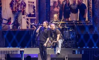 A band performs on stage with bright lights and a large screen displaying images.