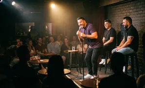 A comedian performs on stage in front of a laughing audience.