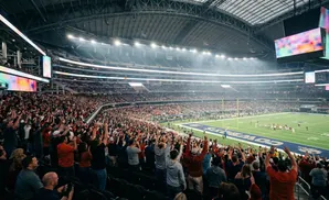 Fans cheer at a football game in a packed stadium with large screens displaying colorful graphics.