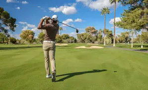 Golfer hitting a ball on a sunny day at a golf course with palm trees.