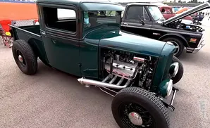 Green hot rod pickup truck with exposed engine and chrome exhaust pipes.