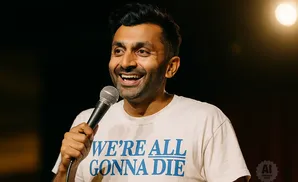 Comedian holding a microphone, wearing a shirt that says 