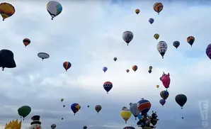 A multitude of colorful hot air balloons fill a cloudy sky, some with unique designs like a unicorn and a snowman.