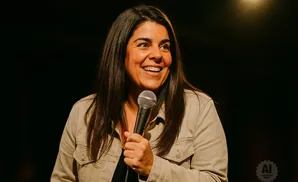 A woman with dark hair smiles while holding a microphone.