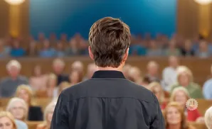 Man in a black shirt faces away from the camera, addressing an audience in a lecture hall.