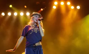 Singer wearing a beret and t-shirt performs on stage with bright lights.