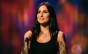 Woman with tattoos and a microphone on a colorful background.