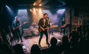 A band performs on a dimly lit stage with bright spotlights and smoke.