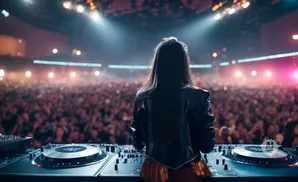 A DJ plays to a large, cheering crowd at a concert, with bright stage lights illuminating the scene.